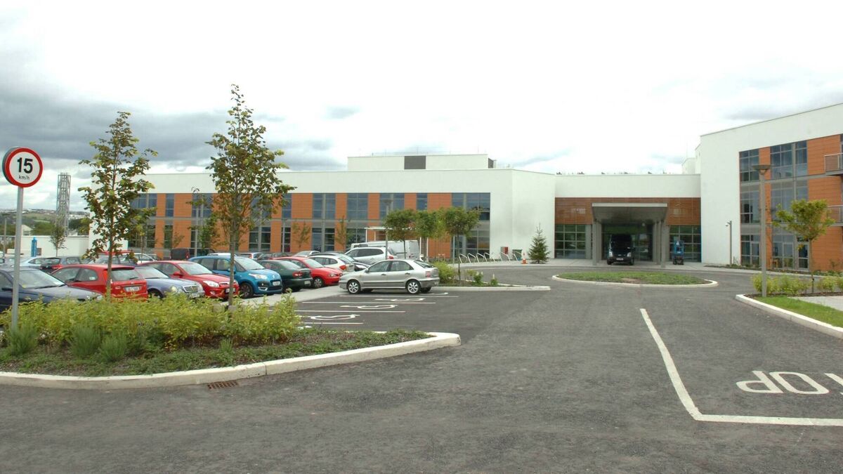 Parking lot with cars, landscaped shrubs, and modern office buildings under cloudy sky.