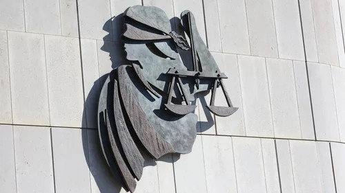 Metal sculpture of a man’s face and hat mounted on a white tiled wall, casting shadows.