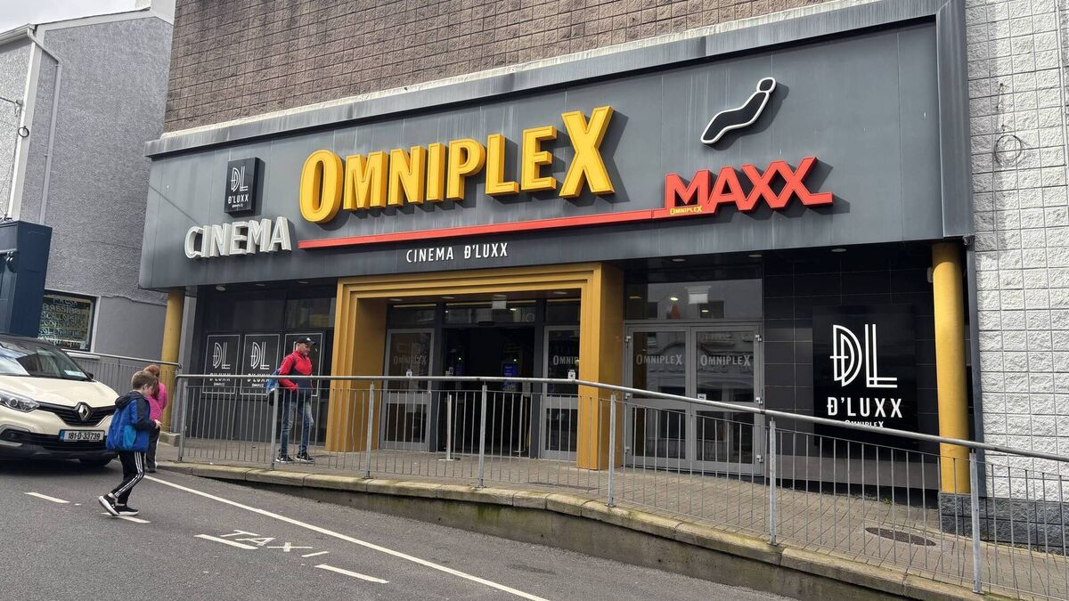 Exterior of Omniplex cinema with OMNIPLEX and MAXX signs, people waiting behind metal railings.