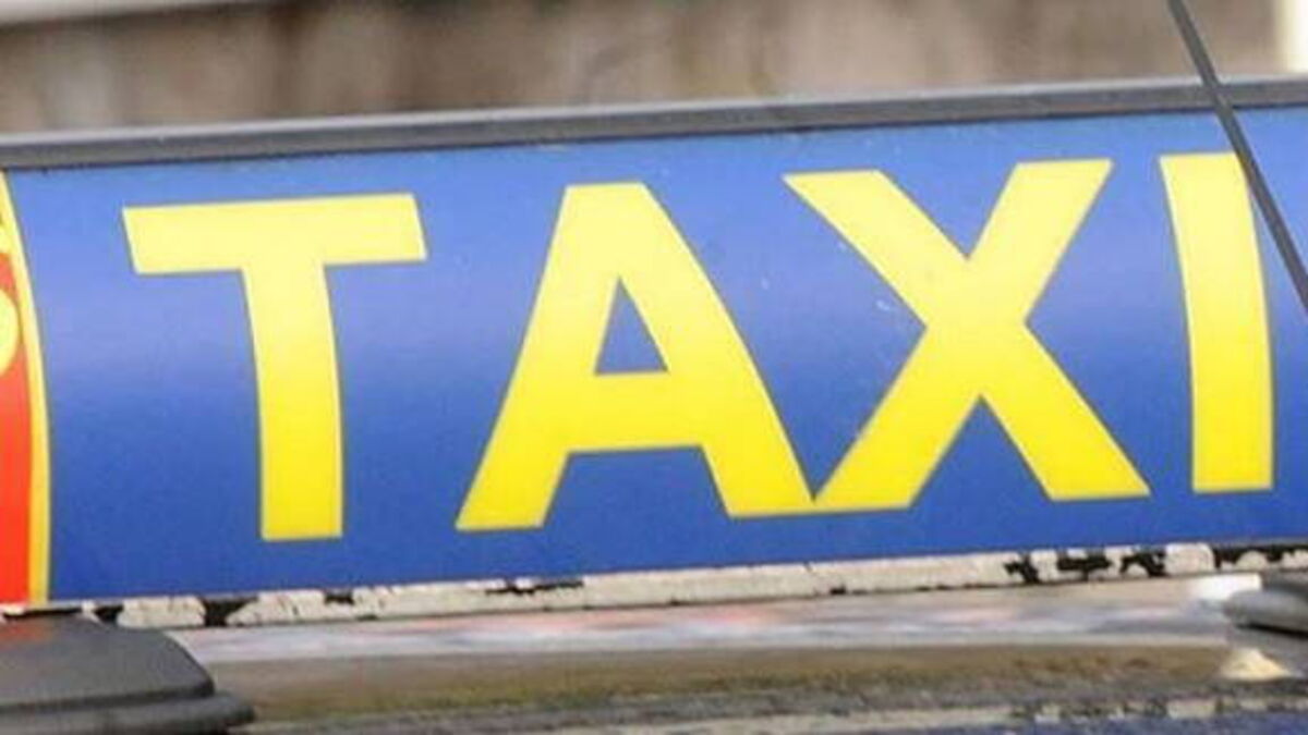 Close-up of a blue sign with large yellow letters reading TAXI, mounted on a street.