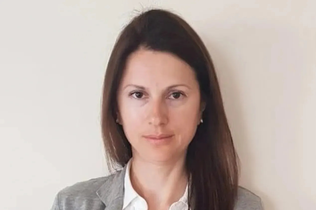 Professional headshot of a woman with long dark hair wearing a gray blazer and white shirt.