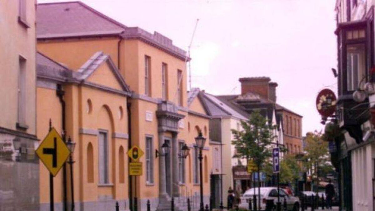 Street scene with European buildings, traffic signs, parked cars, and a cloudy sky in the background.