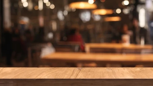 Warmly lit café interior with blurred background and empty wooden table in the foreground.