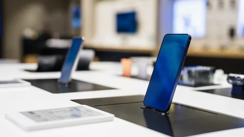 Smartphone on a conference table with blurred office desks and screens in the background.