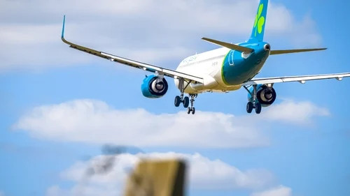 Airplane landing with landing gear down, blue-and-white fuselage, against a cloudy sky background.
